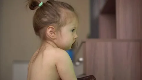 Toddler without clothes eats ice cream in chocolate and watches tv Stock Footage 153132914