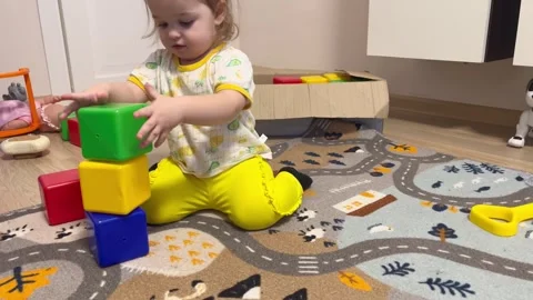 Toddler in yellow pants and patterned shirt stacks colorful building blocks Stock Footage 329913979