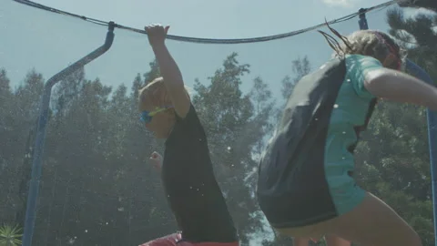 Toddlers bouncing on trampoline playing in summer with water fun Stock Footage 135791810