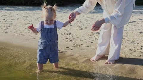 Toddler's first steps into the water at the beach with adult guidance Stock Footage 345364556