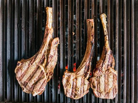 Tomahawk rib beef steak on hot black grill with flames Stock Photos