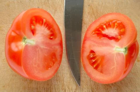 Tomato and blade on brown wooden chopping board Stock Photos