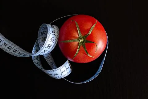 Tomato and a blue meter tape on a black background, concept of healthy eating Stock Photos