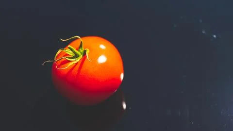 A tomato on black background glassy surface minimalist contrast vibrant colou Foto stock