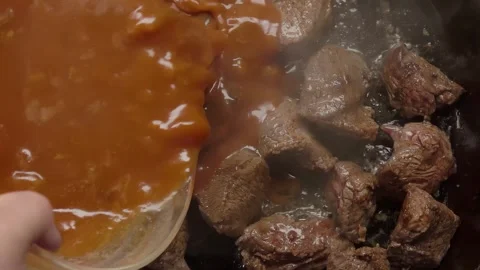 A tomato broth sauce is poured over beef pieces that are stewing in a frying pan Video stock 294720180