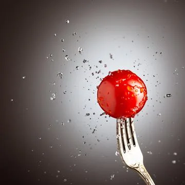 Tomato cherry on a fork in splashes of water. Black white background Stock Photos