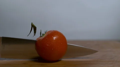 Tomato is cut in half with a large metal knife in slow motion Stock Footage 100008895