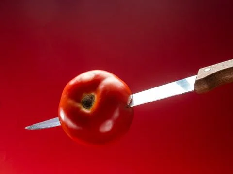 Tomato with knife on red background Stock Photos