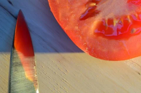 Tomato with a knife on wooden table lit by the sun Stock Photos