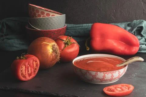 Tomato sauce in a bowl with a spoon on a black slate board with vegetables ar Stock Photos