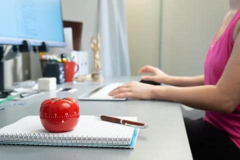 Tomato-shaped kitchen timer on a working desk - time management concept Stock Photos