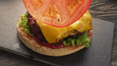Tomato slice is placed on the top of the fresh homemade grilled burger Stock Footage 141457040