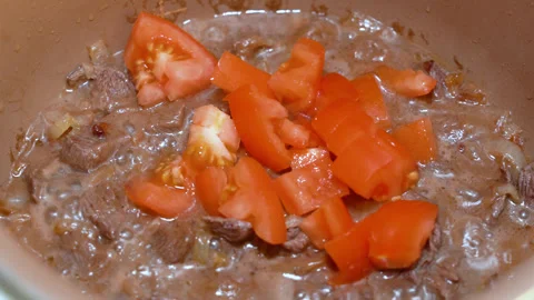 Tomatoes are added to beef that is stewed Stock Footage 247833125