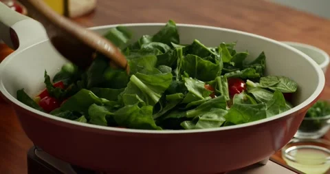 Tomatoes with are fried with green spinach leaves in a non-stick frying pan, the Vídeos de archivo 327974403