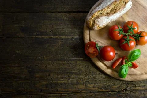 Tomatoes, basil and a rustic bread on a wooden table 库存照片