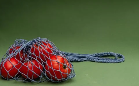 Tomatoes in blue shopping string bag on green background. Eco friendly concep Stock Photos