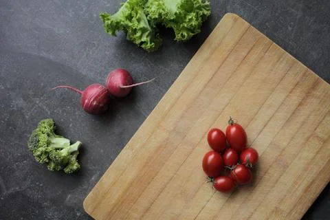 Tomatoes on a cutting board on a gray table and fresh vegetables Stock Photos