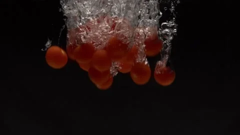 Tomatoes fall into water in slow motion. on a black background Stock Footage 131037433