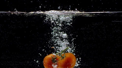 Tomatoes falling into water in slow motion. Isolated on black background. Close Video stock 124833255
