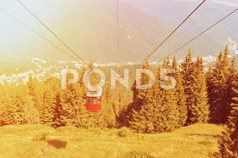 A toned picture of bright red cableway cabin moving to the top of the mountai Stock Photos