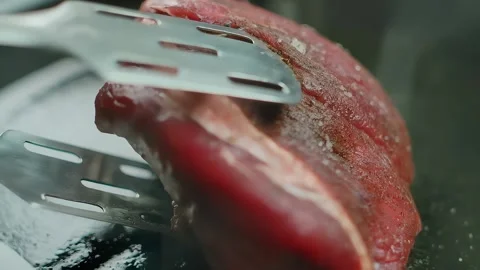 Tongs flip a piece of beef with an appetizing crust Stock Footage 294409631