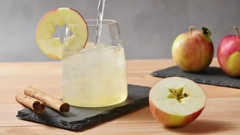 Tonic water pours over apple cider and ice in glass beside apples and cinnamon Stock Footage 345557861