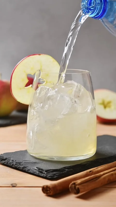 Tonic water pours over apple cider and ice in closeup glass beside fresh apple Stock Footage 345558248