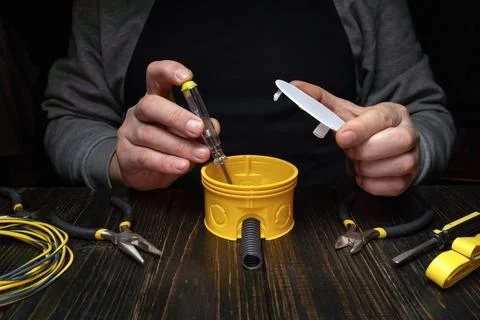 Tool handling and electrical work being done on a yellow junction box at a .. Stock Photos