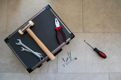 A toolbox with a mallet, wrenches, pliers, and screwdriver on a tiled floor. Stock Photos