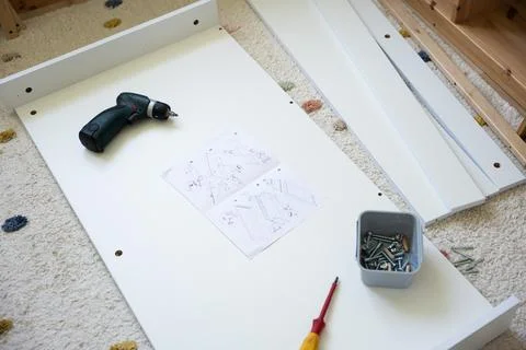 Tools and assembly instructions on white furniture panel with screws and drill Stock Photos