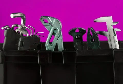 Tools and gadgets in a black toolbox against pink background Stock Photos