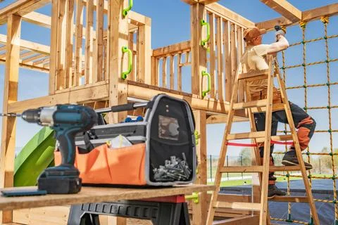 Tools in foreground as a carpenter assembles a garden playset Foto stock