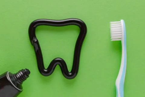 A tooth from black toothpaste, teeth care concept, toothbrush on green Stock Photos