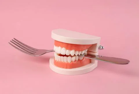 Tooth model with fork and knife on pink background Stock Photos