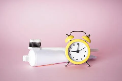 Toothbrush and toothpaste with an alarm clock on a pink background. Dental an Stock Photos