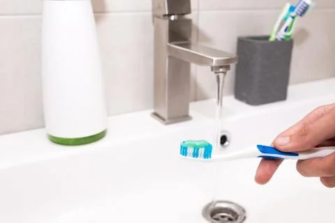 Toothbrush with toothpaste in the guy's hand on the background of the washbasin. Stock Photos
