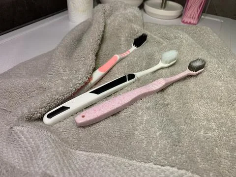 Toothbrushes lying on towel, three different toothbrushes rest on soft gray  Stock Photos