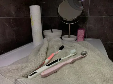 Toothbrushes lying on towel, three different toothbrushes rest on soft gray  Stock Photos