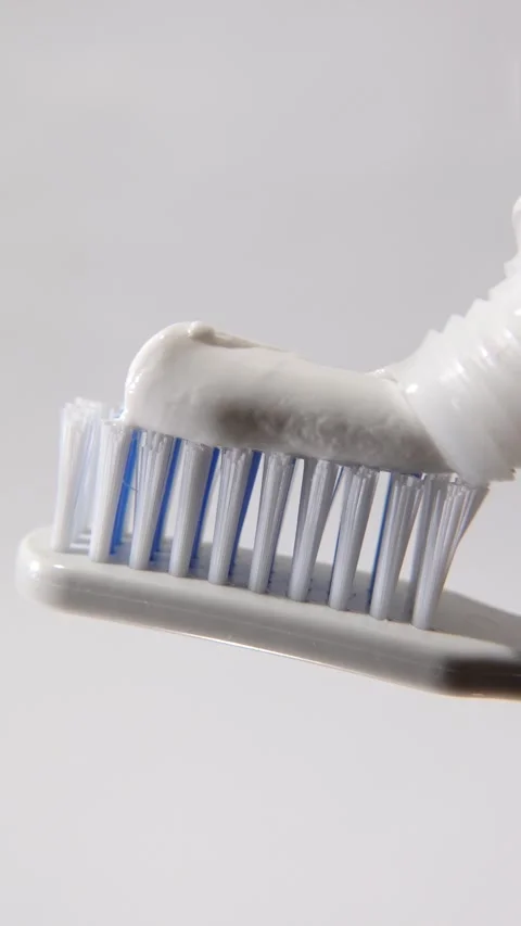 Toothpaste being smoothly applied to the bristles of a toothbrush. Stock Footage 313985891