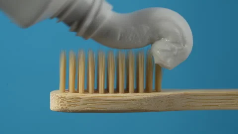 Toothpaste squeezed on the bamboo toothbrush on blue background, close up Stock Footage 305139249