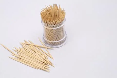Toothpicks in a Clear Plastic Container with Scattered Toothpicks on a Whit.. Foto stock