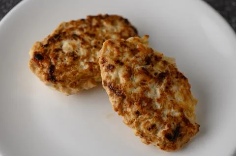 Top-angle close-up photograph of two pan-fried meat cutlets on a white plate Stock Photos