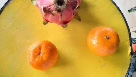 Top angle, Two oranges and a red dragon fruit on a yellow barrel 01 Stock Photos