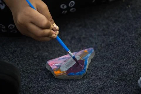 Top Angle View of Hand Applying Dark Purple Paint to Triangular Rock with B.. Stock Photos