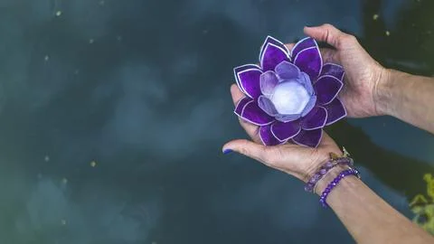 Top angle view of hands holding a purple glass lotus over water. Yoga and m.. Foto stock