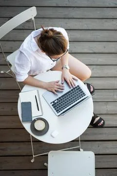 Top angle view of woman while using laptop on summer wooden terrace, coffee on Stock Photos