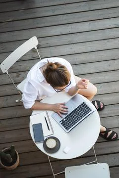 Top angle view of woman while using laptop on summer wooden terrace, coffee on Stock-Fotos
