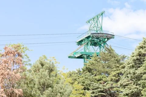 The top of the cable car post is visible from the trees against the blue sky 스톡 사진