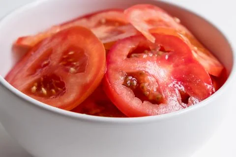 Top diagonal close up view of sliced tomatoes in white bowl on white counter  Stock Photos