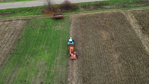 Top down 4K aerial of tractor tilling between harvested and green fields Video stock 322933790